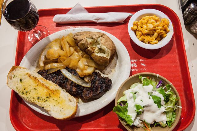This is a photo of steak, a baked potato, wine, Mac 'n cheese, and salad on a red tray at Tad's Steaks.
